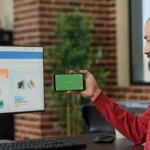 male-worker-holding-smartphone-with-horizontal-green-screen-business-office-young-adult-working-with-blank-chroma-key-isolated-template-with-mockup-background-mobile-phone-display